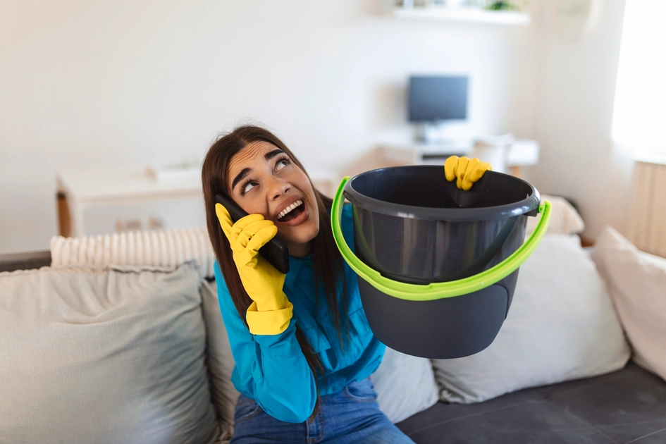 shocked-woman-calling-plumber-while-collecting-water-leaking-from-ceiling-using-utensil